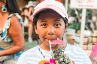 A child holding a drink made of a pineapple and sipping from a straw