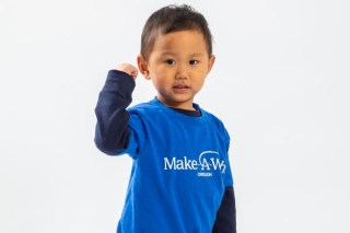 A young child pumping his fist while wearing a Make-A-Wish blue t-shirt