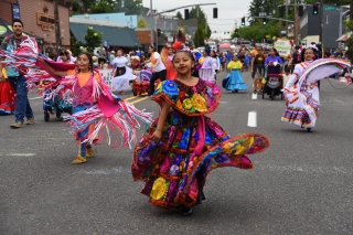 A girl in a brightly colored dress dancing at the Portland Rose Festival Junior Parade