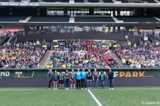 AdoptOneBlock group photo of volunteers sitting in the stands of a soccer stadium