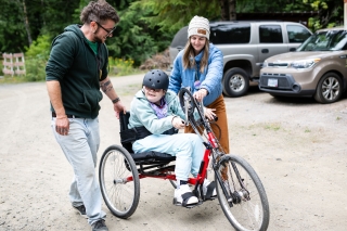 A person with a disability riding a three-wheel bicycle assisted by two other people