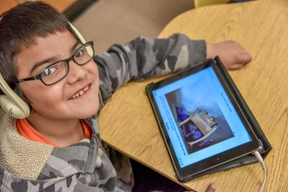 A child with headphones on and watching an animation on a tablet